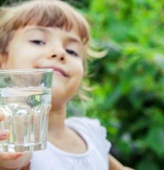 Glimlachend kind steekt een glas met water vooruit